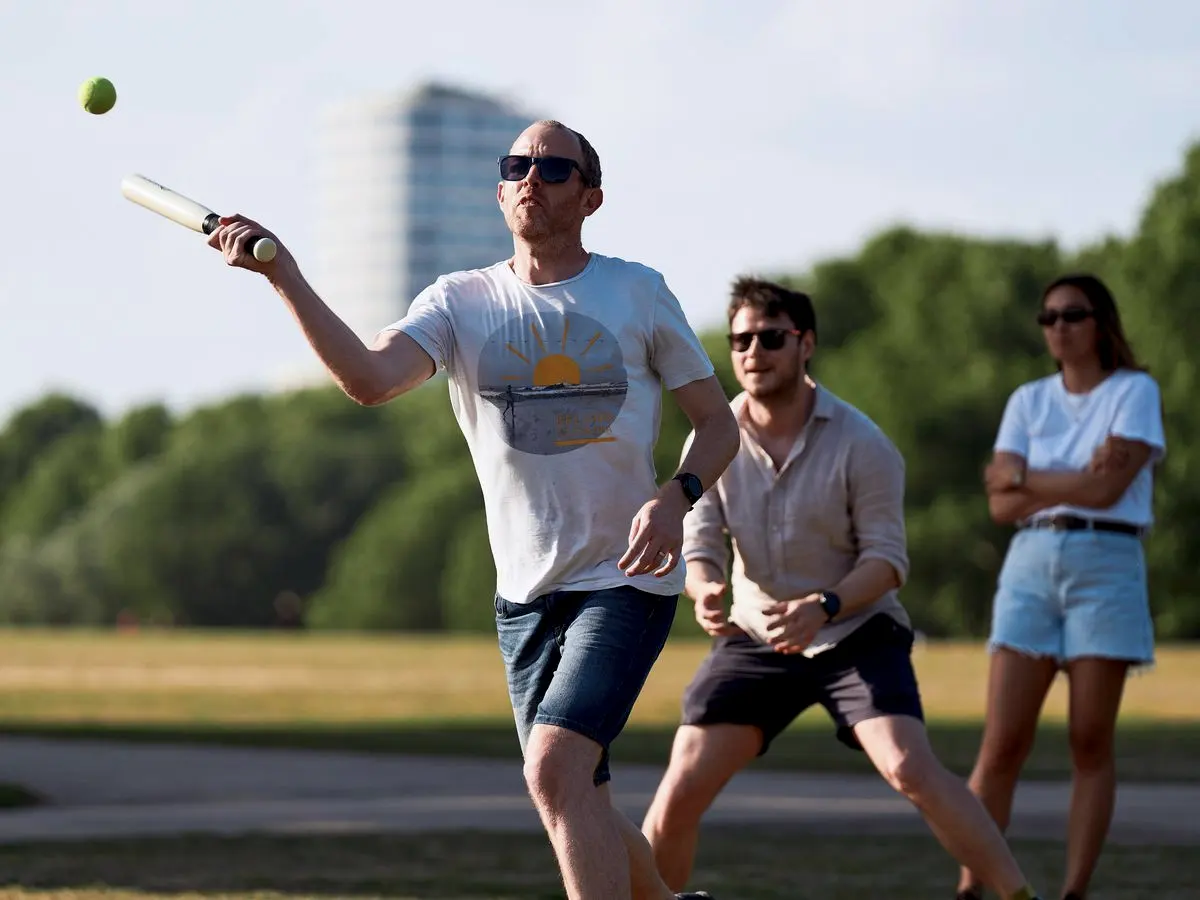 A teammate hitting the ball at rounders, with two more behind